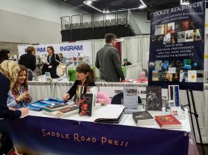 Tania reading cards on blue silk at the Saddle Road Press table at AWP 2019